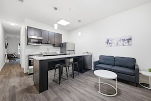 Een moderne keuken met een centraal eiland, barkrukken en een grijze bank in een woonruimte.