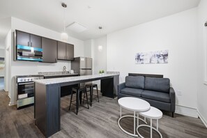 Eine moderne Küche mit Kochinsel, Barhocker, Backofen und grauem Sofa mit Couchtisch.