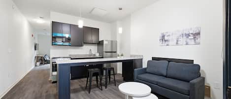 Una cocina moderna con armarios oscuros, una isla central y un sofá gris con una mesita de centro blanca.