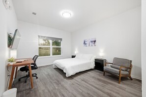 Ein modernes Schlafzimmer mit Bett, Schreibtisch, Stuhl und Fenster.