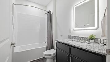 Une salle de bain moderne équipée d’une baignoire, de toilettes et d’un meuble-lavabo avec un évier et un miroir.