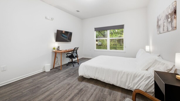 Een slaapkamer met een bed, een bureau, een stoel, een televisie en een raam met uitzicht op bomen.