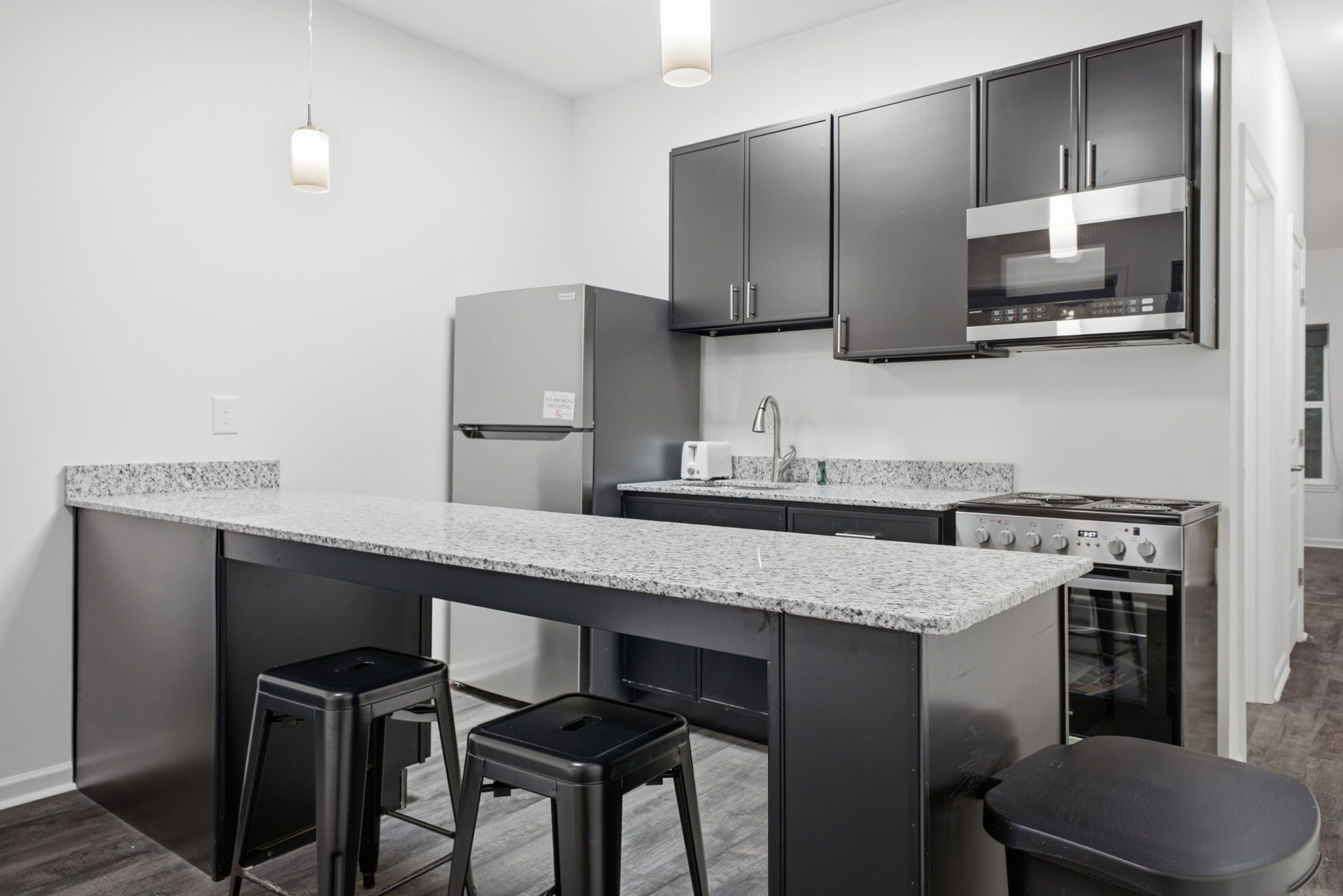 A modern kitchen with a central island, bar stools, a built-in oven, and stainless steel appliances.