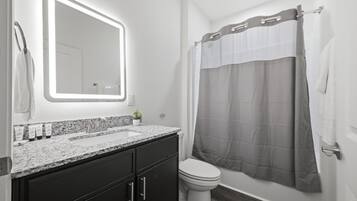 Een moderne badkamer met een granieten aanrechtblad, donkere kastjes, een wit toilet en een douchegordijn.