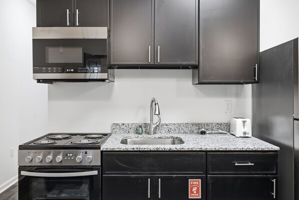 A modern kitchen with a gas stove, oven, stainless steel sink, and dark cabinets.