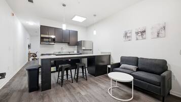 A modern kitchen with a central island, bar stools, a grey sofa, and a round coffee table.