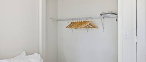 Ein Schlafzimmer mit einem Bett, einem Schrank mit Holzgalgen und einer weißen Wand.