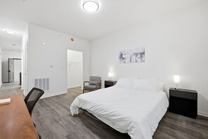 Habitación de hotel con cama, dos mesitas de noche, una silla, un escritorio y un cuadro en la pared.