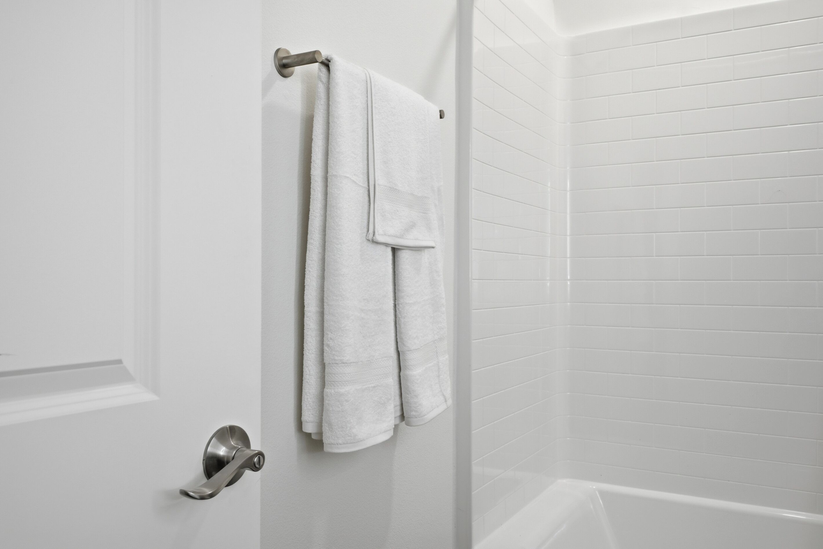 A bathroom with white tiled walls, a white bathtub, and a towel hanging on a metal towel rack.
