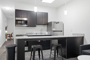 Een moderne keuken met donkere kastjes, roestvrijstalen apparatuur, een granieten aanrecht en barstoelen.