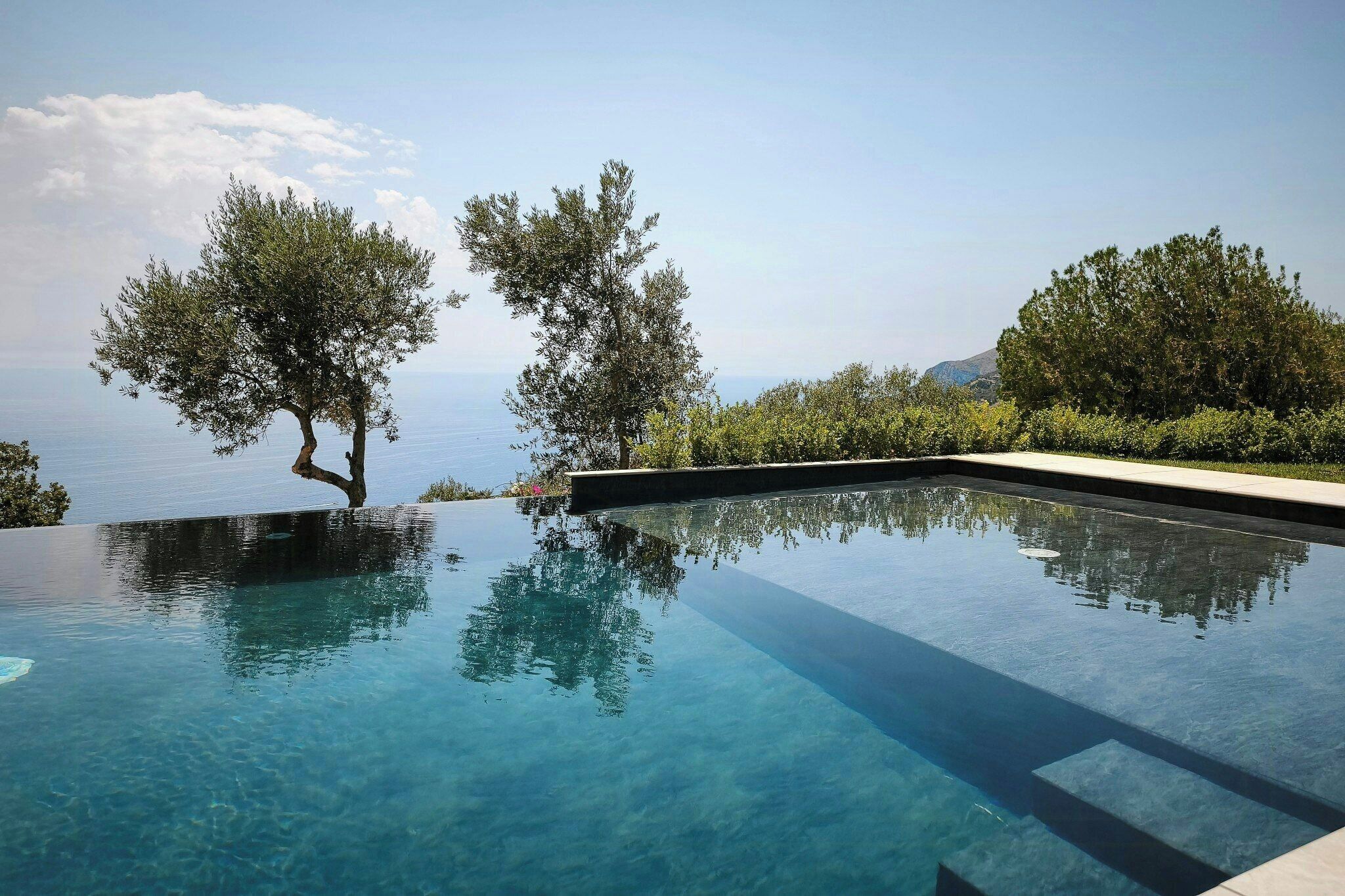 Ein Pool ohne Ende mit klarem Wasser, umgeben von Bäumen und Blick auf das Meer.