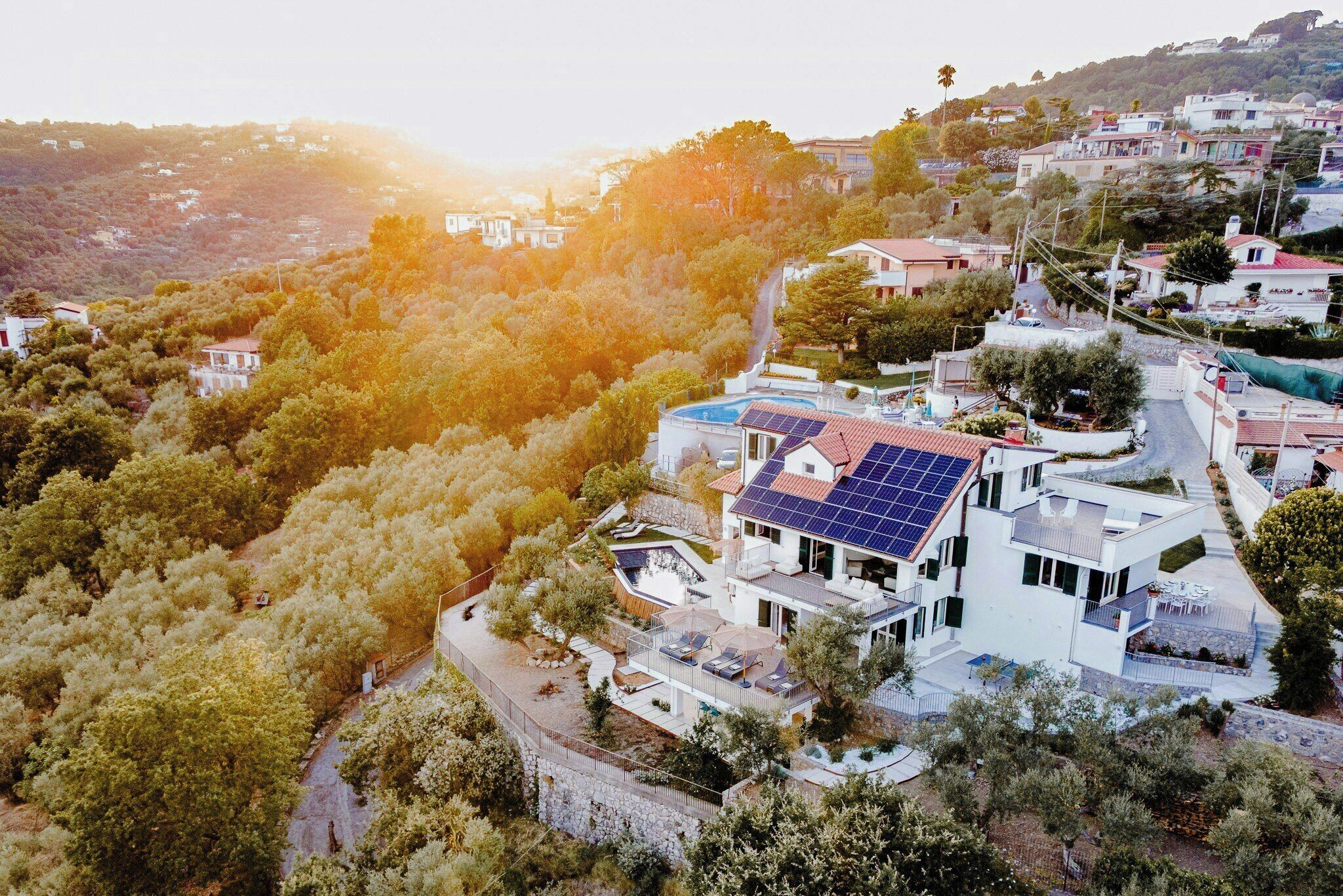A modern house with a swimming pool, solar panels, and a view of a hilly area.