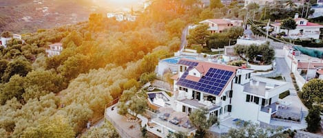 A modern house with a swimming pool, solar panels, and a view of a hilly area.