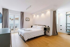 Een moderne slaapkamer met een bed, nachtkastjes, een flatscreen televisie en een balkon met uitzicht.