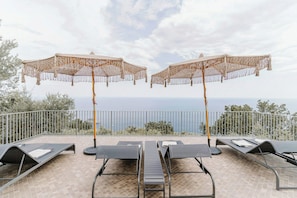 A terrace with sun loungers and two large woven umbrellas, overlooking a coastal view. - Villa near Monte San Costanzo with pool (Massa Lubrense)