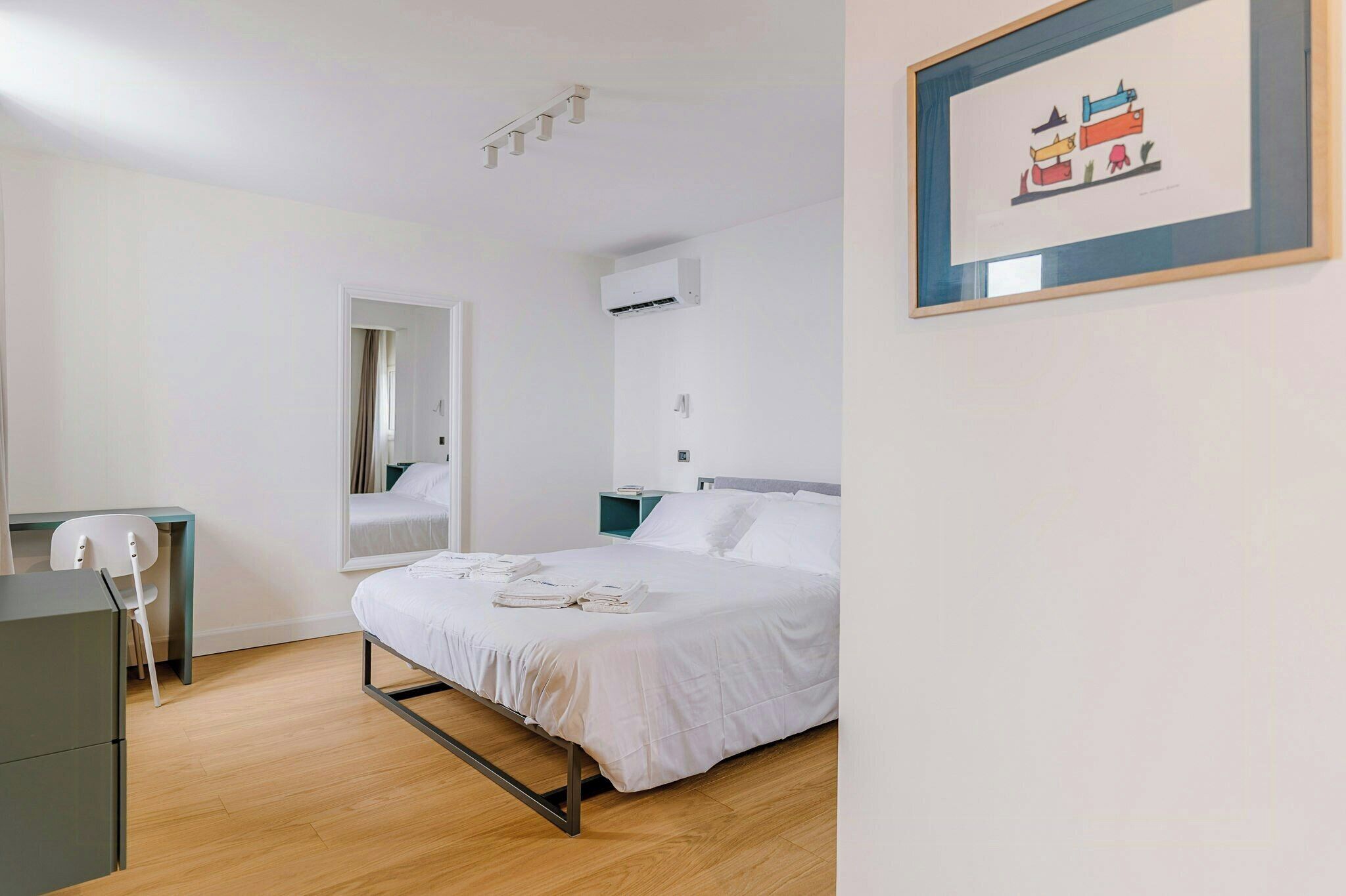 A hotel room with a bed, a desk, a chair, and a framed picture on the wall.