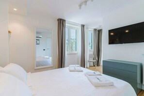 Een hotelkamer met een groot bed, een flatscreen televisie, een spiegel en een raam met gordijnen.