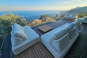 A terrace with two white sofas and a wooden table, overlooking a coastal landscape. - Villa near Monte San Costanzo with pool (Massa Lubrense)