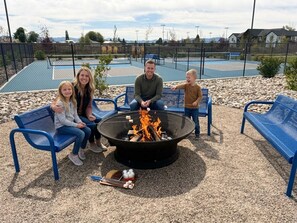 A family sitting on blue benches around a fire pit with a pool in the background.