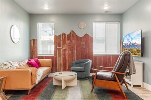 A living room with a sofa, armchair, and coffee table, a wooden accent wall, and a painting on the wall.