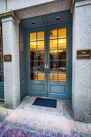 Une entrée avec une double porte, un paillasson, une plaque de numéro et une enseigne indiquant « The Alexandre ».