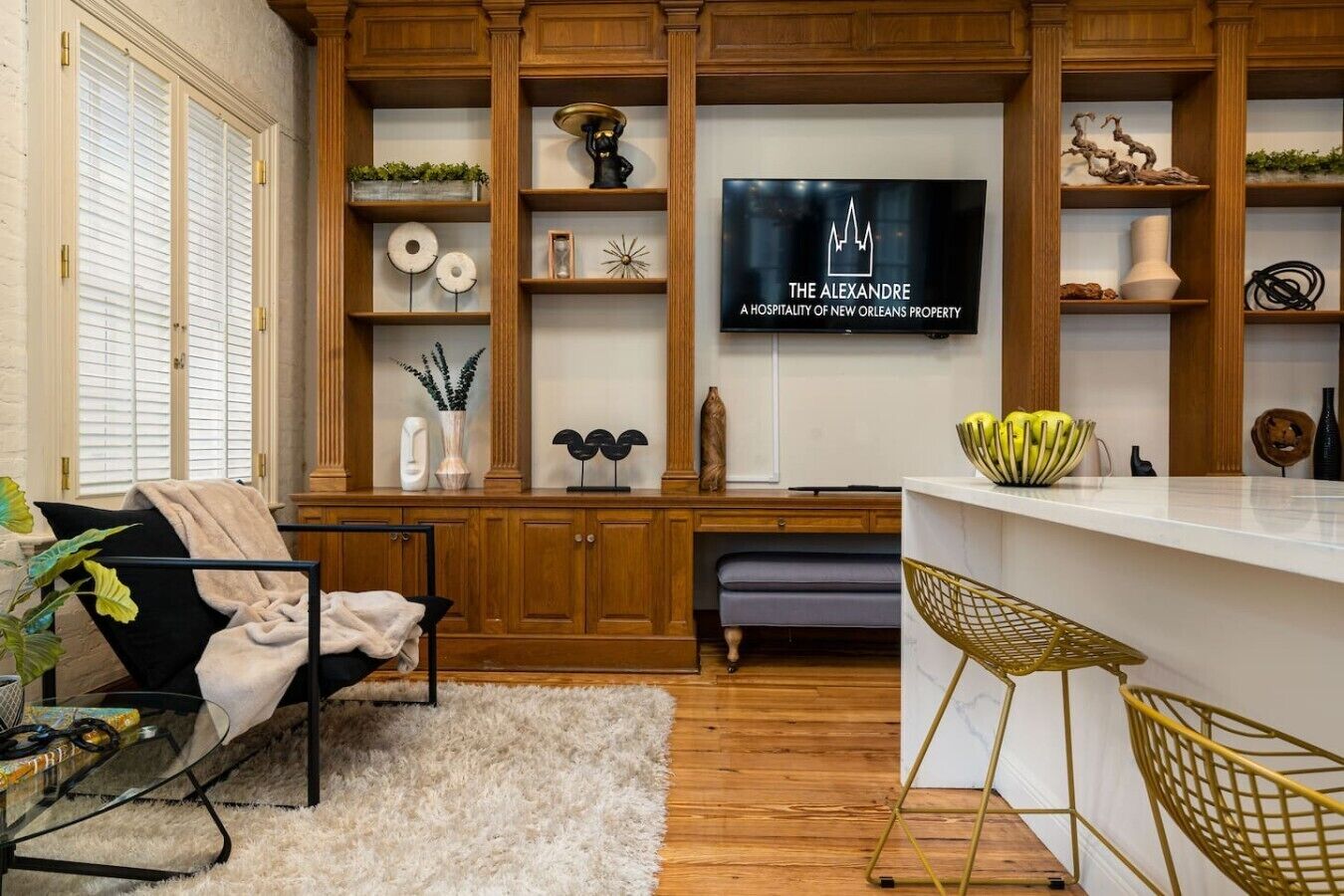 Una sala moderna con una televisión de pantalla plana montada en una pared de madera, un sofá con una manta decorativa, una mesa de centro y un comedor con una barra.