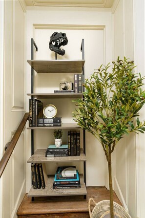 Un escalier en bois avec une rampe en métal, une petite plante en pot et une bibliothèque contenant des livres et une horloge.