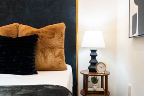 Un lit avec deux oreillers, une table de chevet avec une lampe, une horloge et une petite plante.