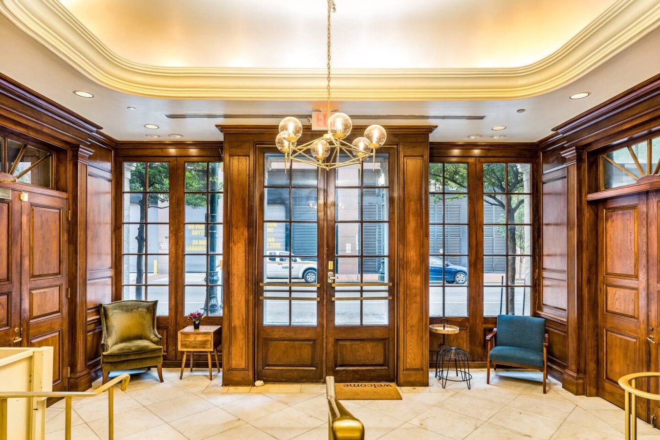 Un hall d’entrée agrémenté d’un magnifique lustre, de portes en bois et offrant une vue sur la rue.