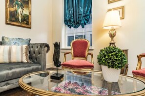 A living room with a sofa, a red upholstered chair, a glass coffee table, a potted plant, and a painting on the wall. - Elegant 1BD Condo | NOLA Walkable Escape (New Orleans)