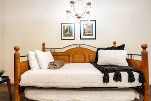 Ein Bett mit hölzernem Kopfteil, weißer Bettwäsche und einem aufgerollten Handtuch. An der Wand über dem Bett befinden sich zwei gerahmte Bilder.