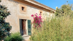 A courtyard with a table and chairs, a covered bench, a potted plant, and a building with a tiled roof. - Room 'Suite Summer' with Shared Pool, Wi-Fi and Air Conditioning (Alaró)