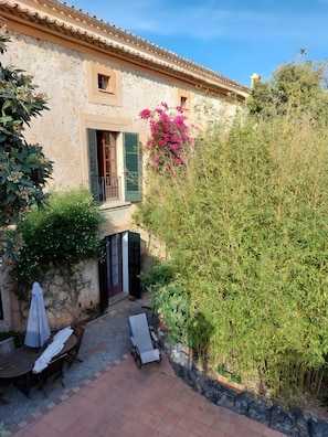 A courtyard with a table and chairs, a covered bench, a potted plant, and a building with a tiled roof. - Room 'Suite Summer' with Shared Pool, Wi-Fi and Air Conditioning (Alaró)