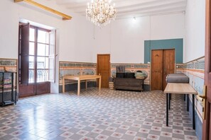 Um quarto espaçoso com uma grande janela, um lustre, uma mesa de madeira e piso estampado.