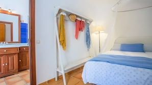 A bedroom with a bed, a nightstand, a mirror, and a clothing rack with various garments. - Room 'Suite Summer' with Shared Pool, Wi-Fi and Air Conditioning (Alaró)