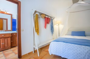 A bedroom with a bed, a nightstand, a mirror, and a clothing rack with various garments. - Room 'Suite Summer' with Shared Pool, Wi-Fi and Air Conditioning (Alaró)