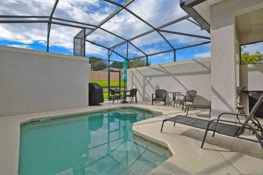 An indoor pool area with a glass enclosure, lounge chairs, and a barbecue grill.