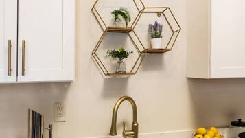 A kitchen with white cabinets, a stainless steel sink, and a gold faucet. There are three hexagonal shelves with plants and a bowl of lemons on the counter.