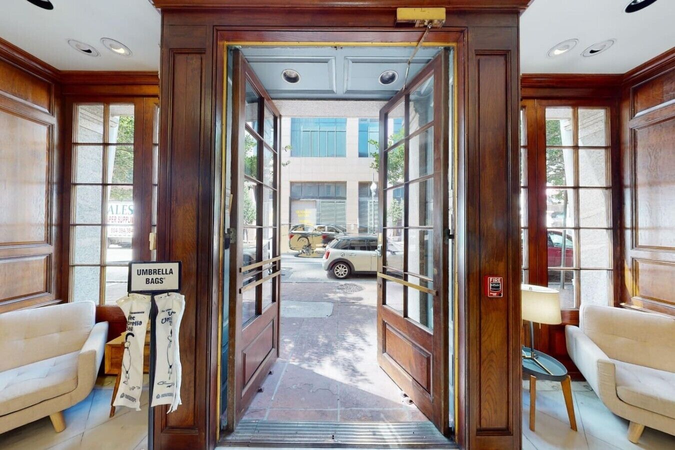 A hotel entrance with a wooden door, a fire alarm sign, and a view of parked cars outside.