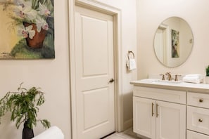 Een badkamer met een witte deur, een wastafel met gouden details, een spiegel en een potplant.