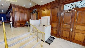 A hotel lobby with a staircase, wooden paneling, and a reception area.