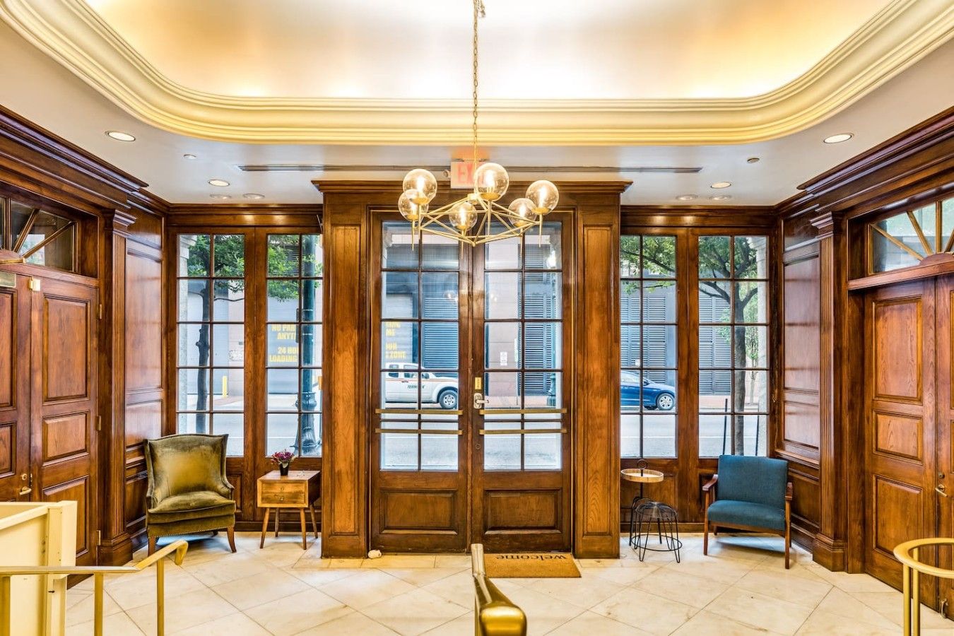 A lobby with a grand chandelier, wooden paneling, and a view of the street outside.