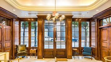 A lobby with a grand chandelier, wooden paneling, and a view of the street outside.
