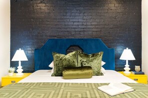 Een bed met een blauw hoofdeinde, twee kussens, een groene plaid en een boek op de nachtkastje.