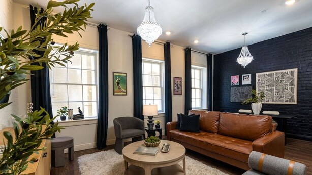 A modern living room with a brown leather sofa, a round coffee table, and a chandelier. - 2BD/2BA in NOLA’s Best Walkable Neighborhood (New Orleans)