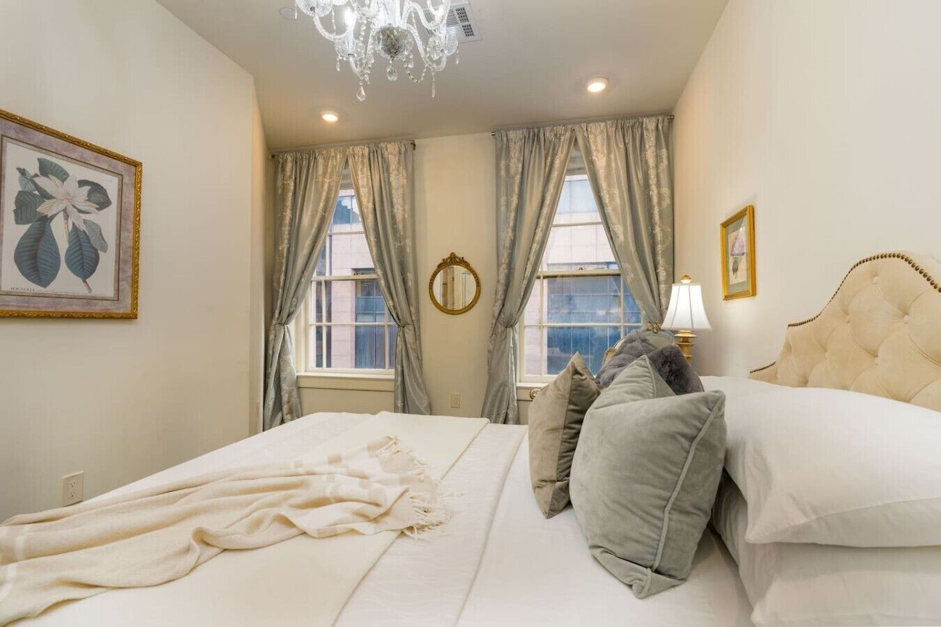 A bedroom with a bed, pillows, a chandelier, and a window with curtains.