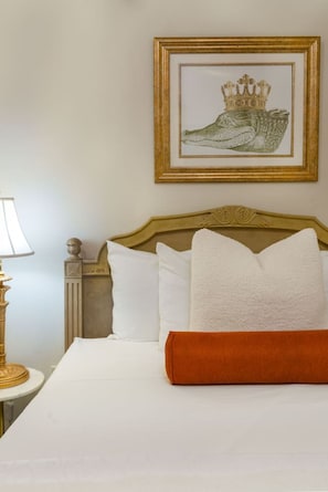 A hotel room with a bed, pillows, a framed picture on the wall, a lamp, and a decorative headboard. - Central 2BR Retreat | Bourbon & Streetcar Steps (New Orleans)