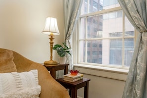 A bedroom with a bed, a bedside table with a lamp, a potted plant, and a window with curtains. - Central 2BR Retreat | Bourbon & Streetcar Steps (New Orleans)