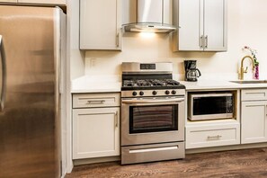 A kitchen with a stainless steel refrigerator, a gas stove, an oven, a microwave, and white cabinetry. - Central 2BR Retreat | Bourbon & Streetcar Steps (New Orleans)