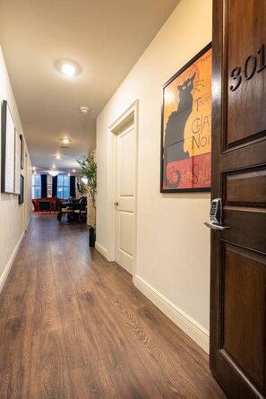 A hallway with a wooden floor, a door with a number, and a poster on the wall. - Walk to Bourbon | Spacious & Bright 2BD in CBD (New Orleans)